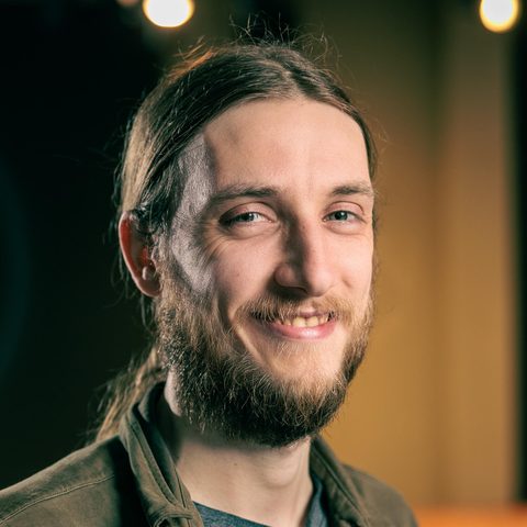 Floris van Beers, smiling, with long hair tied back and a beard, wearing an olive jacket.